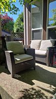 Outdoor patio furniture chair and loveseat under shaded patio showing brown woven synthetic wicker frames with beige cushions