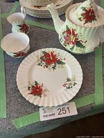 Overview photo showing the teapot, creamer, sugar bowl, and one side plate with poinsettia decoration on a grey surface.