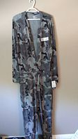 Full view of SAXX Nightcrawler onesie hanging on a hanger, displaying gray camo and skull pattern, size medium tag visible.