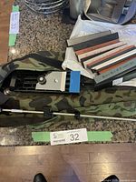 Overall view of sharpening stones, jig, metal guide rod, and camouflage carrying case on countertop.