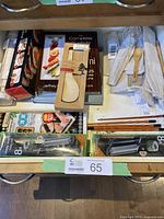 Drawer containing sushi making accessories including wooden spoons, chopsticks, sushi rollers, bamboo mats, and cookbooks.