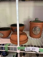 Set of two Val-do Sol terra-cotta mixing bowls, flour cannister, and garlic cooker arranged on a metal shelf.