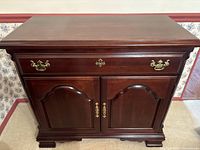 Front view of traditional wooden sideboard showing rich dark wood finish, brass drawer handles, and two arched panel cabinet doors with brass pulls.