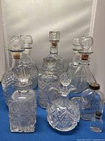 Front view showing all glass decanters and bottles with stoppers and corks on blue background.