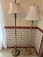 Full view of two brass floor lamps standing side by side, showing height, pole, and fabric shades