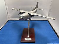 Front view of the silver metallic Fairchild C-123 model airplane with black propellers and US Air Force markings on the wings, mounted on its wooden stand with metal support.