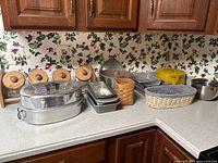 Photo of kitchen countertop showing wooden canisters, metal steamer, baking pans, wicker baskets, and mixing bowls