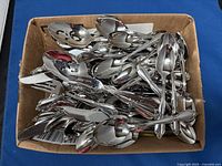 Box containing approximately 50 pieces of stainless steel flatware including forks, spoons, knives, and serving spoons with floral patterned handles.