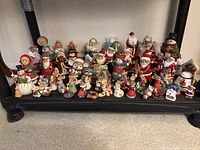 Front view of multiple Christmas figurines arranged on a black shelf showing variety including Santas, angels, animals, and snowmen in red, green, white colors.