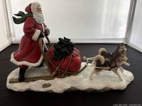Side view of the Alaskan Sled Ride figurine showing Santa, sled with red sack, and two husky dogs on snow-like base.