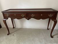 Front view of the traditional dark brown wooden sofa table with two drawers, showing brass handles and scalloped detailing on legs and apron.