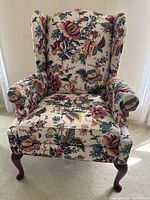 Front view of wingback chair showing multicolor floral fabric and wooden cabriole legs.