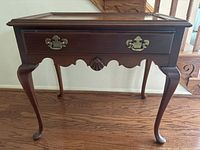 Front view of wooden side table showing decorative drawer with brass hardware and carved shell detail, cabriole legs.