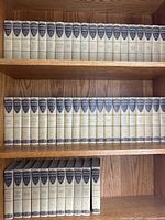Three shelves displaying 51 volumes of Harvard Classics in cream cloth bindings