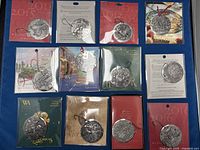 Set of 12 Wendell August metal Christmas ornaments in original packaging showing diverse holiday-themed embossed metal designs including festive bells, home scenes, and traditional motifs.