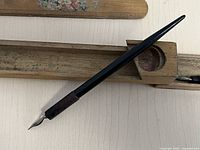 Close-up of a black fountain pen with wooden grip section and silver metal nib resting on the inside of the wooden case.