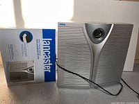 Photo of Lancaster air purifier model KJ25FE-A with its power cord visible alongside a new Lancaster replacement filter box.