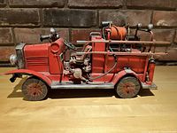 Side view showing detailed metal construction, fire hose reel on top, and ladder along the truck's right side.