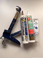 Top view of blue metal caulking gun with three tubes of caulking on white background.