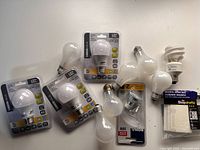 Various LED and incandescent lightbulbs, plus a compact fluorescent bulb and accessories shown on a white surface.