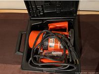 Electric router coiled with power cord inside black hard plastic case.