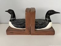 Front view of ceramic loon bookends together, showing black and white painted ceramic loons with red eyes on brown wood bases.