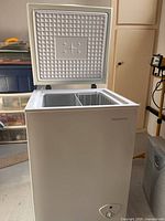 Open lid view of white Insignia chest freezer showing textured pattern and star design on inner lid and wire basket inside.