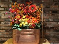 Front view of copper boiler filled with artificial flowers against brick wall