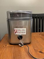 Front view of Cuisinart ice cream maker with clear lid and control knob, showing branded label with product details.
