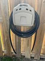 Black rubber hose coiled around beige AMES hose hanger on wooden fence.