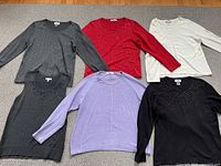 Six women's long sleeve tops laid on carpet, showing variety of colors and sparkle decoration.