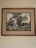 Full view of the framed print showing the stone house artwork, wooden frame with gold trim, and beige mat board.