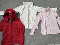 Red hoodie, white sweatshirt, and light pink quarter-zip pullover laid out flat, showing full fit and color.