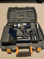 Open case showing cordless hammer drill, two batteries, charger and side handle inside foam cutouts