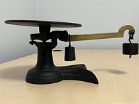 Front-angle view of black metal vintage weigh scale showing round weighing platform and counterweights on arm.