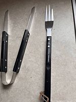 Barbecue fork and tongs laid side by side on a countertop, showing the handles and metal parts prominently displaying the Montréal Canadiens logo and text.