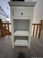 Front view of white night stand showing drawer and two shelves