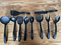 All 10 black Paderno kitchen utensils laid out on wood surface showing full set.