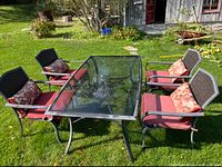 Overview of glass-top table and four of six chairs with cushions on lawn