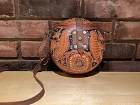 Front view of round wooden purse with carved and painted bird and floral designs, leather strap visible.