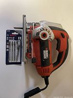 Black & Decker cordless jigsaw with Bosch blade set beside it, showing the entire jigsaw and blade pack for scale and completeness.
