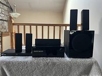 Front view of the Samsung surround sound system components showing the BluRay player, AV receiver, center speaker, subwoofer with two satellite speakers on top, and additional speakers.