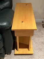 Side view of wooden side table next to dark green leather sofa, showing the thickness of top panel and leg structure.