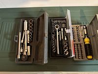 Two open plastic cases containing various socket sets, ratchets, socket extensions, screwdriver handle with bits, and extra mixed sockets