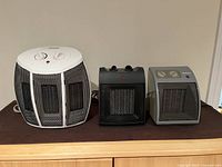 Three electric space heaters displayed side by side on wooden surface, showing front and top controls.