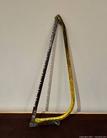 Yellow metal bow saw standing vertically against a wall showing overall shape and blade.