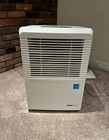 Front view of white UBER Haus dehumidifier showing air vent grill and brand label on lower right corner.