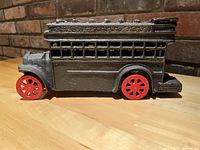 Side view of vintage cast iron double decker bus with red wheels on wooden table against brick wall background.