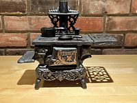 Front view of the miniature cast iron stove displaying the detailed front panel with 'Crescent' branding and decorative legs.