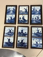 Front view of six wooden framed sets, each with two blue and white ceramic tiles depicting windmills and countryside scenes